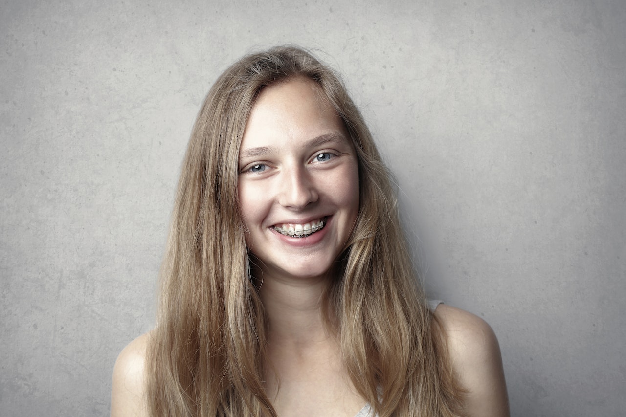 A white teenage girl with braces smiles in a headshot at Lacombe Smiles Dental, the premier dental clinic in Lacombe, Alberta. Our expert dentists use the latest dental technology to provide exceptional dental care services, including teeth cleaning, braces, and fillings. Trust us to keep your teeth and gums healthy and beautiful. Book your appointment today. SEO keywords: dental clinic, Lacombe, Alberta, braces, teeth cleaning, fillings, dental technology, premier dental clinic.